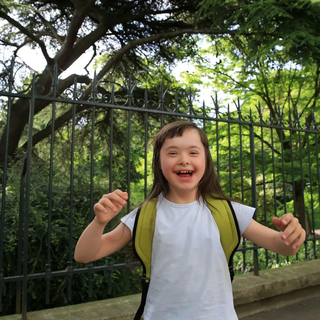 Fröhliches Kind mit Down-Syndrom im Sommer. T-Shirt und Rucksack.