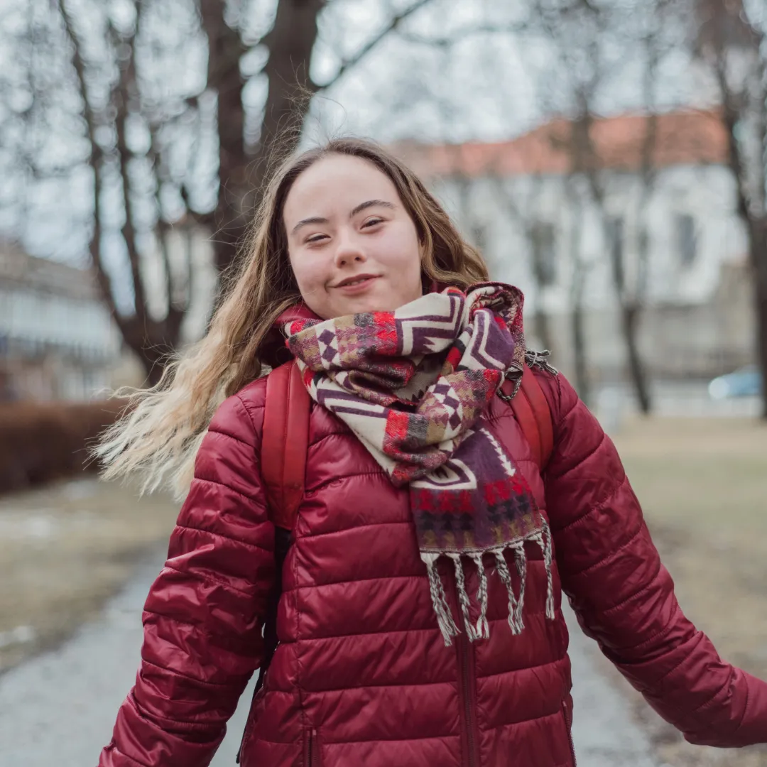 Junge Studentin mit Down-Syndrom, draußen mit roter Jacke